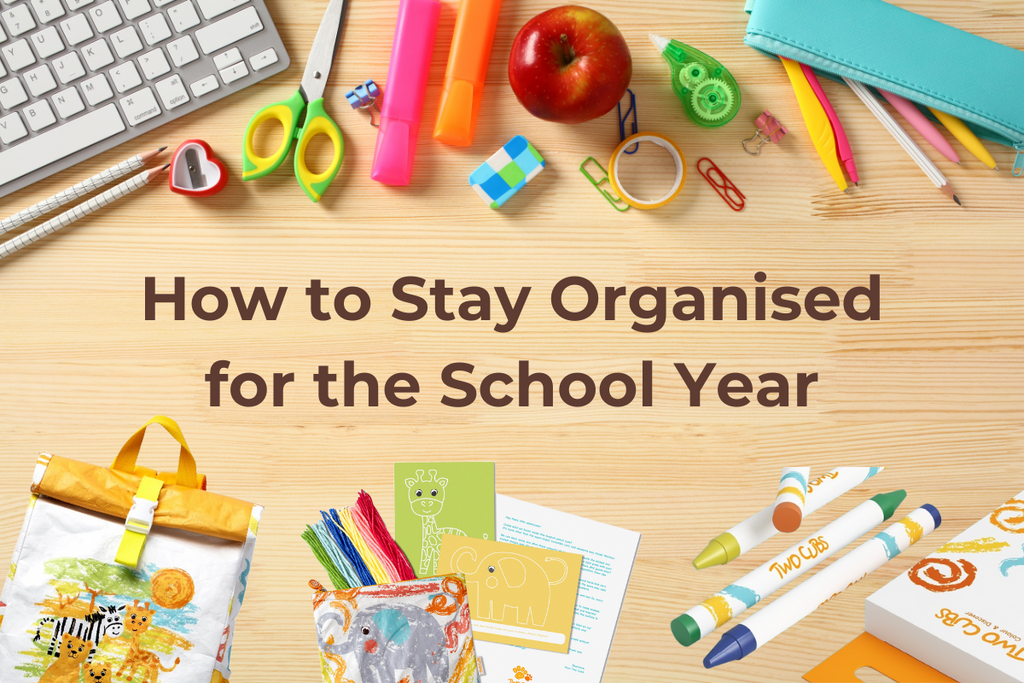 Flat lay of back-to-school essentials, including a TWO CUBS safari backpack, wet bag, crayons, stationery, and activity cards, arranged on a wooden desk. 