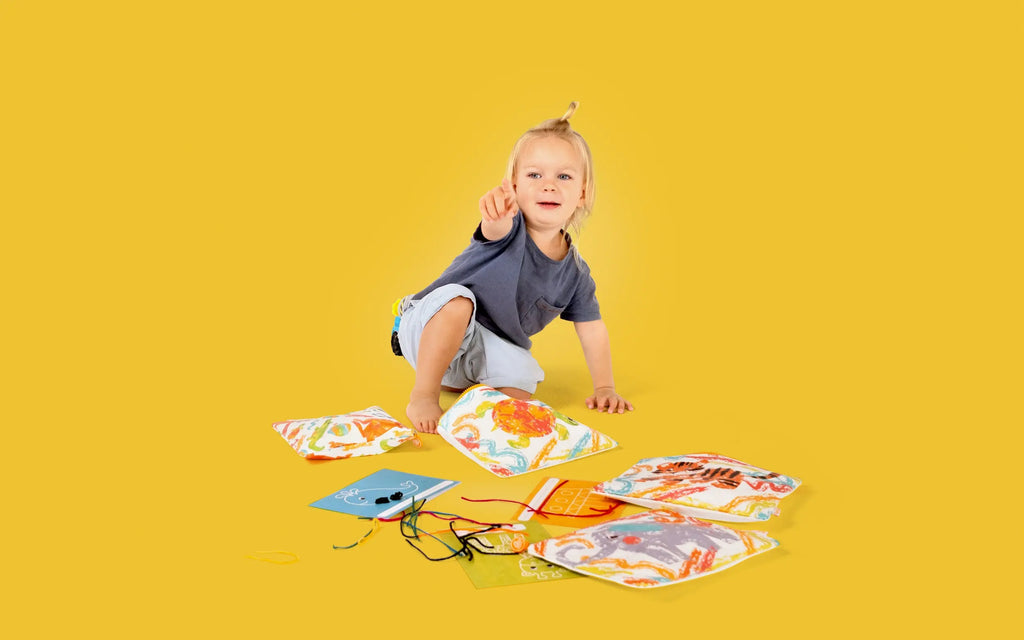 A young child excitedly playing with Two Cubs Crafty Curls, creating colorful art using wax sticks and activity cards on a vibrant yellow background